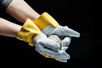 Hände mit Handschuhen halten einen Stein